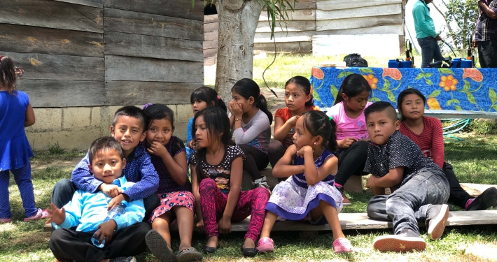 A group of young children sitting on the grass in the shade