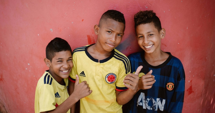 Three young boys wearing football clothing smiling at the camera and giving a thumbs up
