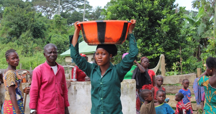 A woman carrying water in a plastic container on her head, Guinea